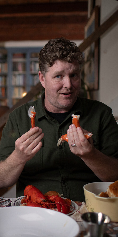 A man holds up two pieces of lobster, demonstrating how to eat them.