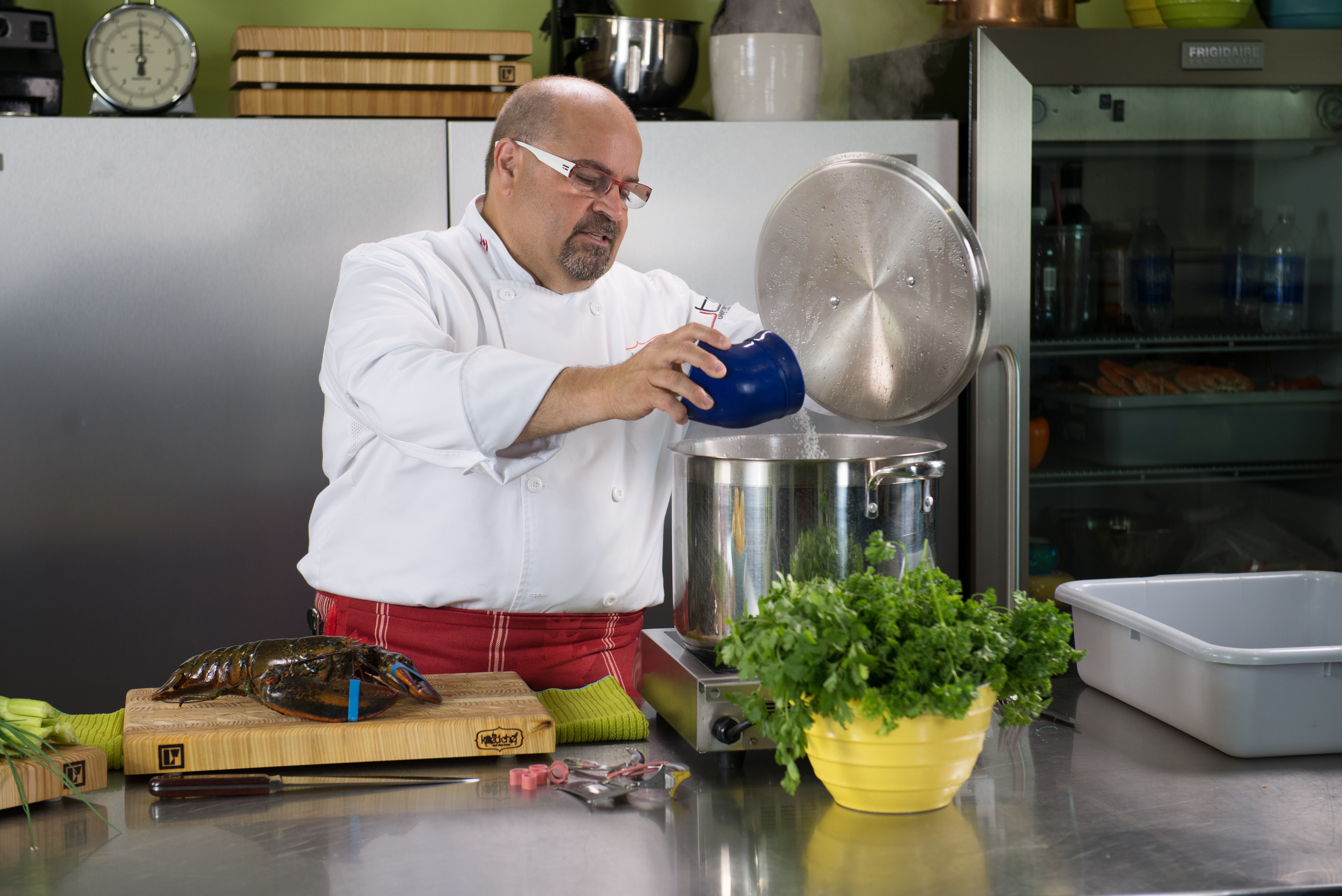 A photo of a male chef pouring salt into a pot to cook lobster.